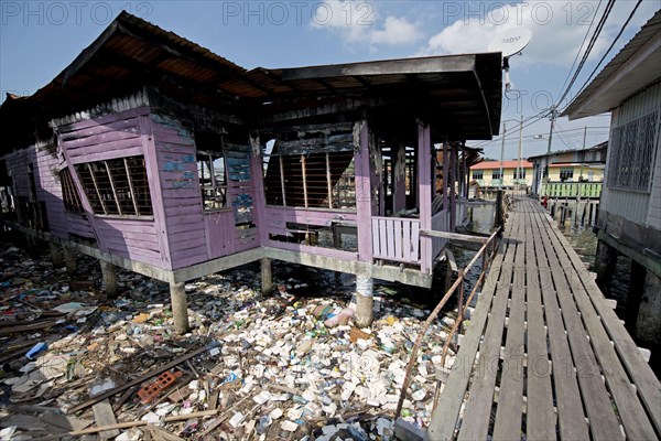 Walkway and burnt-out hut on stilts with waste washed up from the river