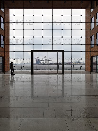 Young man standing in front of modern glass facade with large door and looking at the harbour