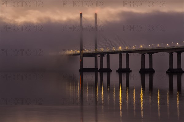 View of road bridge over misty river at sunrise