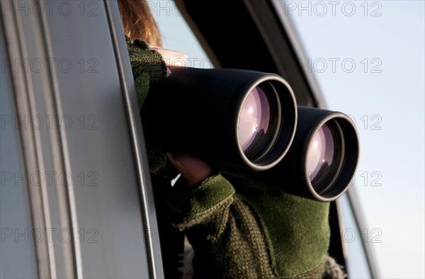 Person looking at wildlife through binoculars from inside car