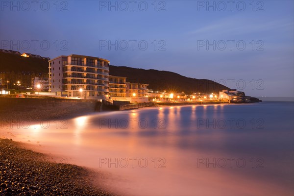The sea rushes in over pebbles on the beach below the seafront promenade in front of sunrise