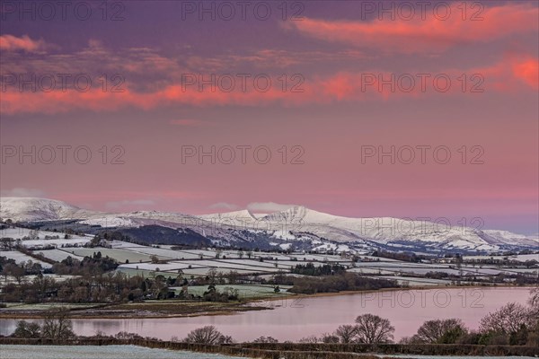 View of snow covered farmland and hills at sunrise