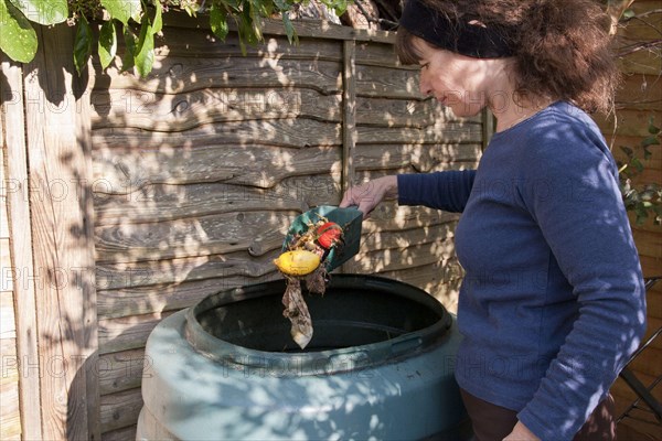 Woman throws vegetable waste into the compost bin in the garden