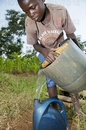 Child draws water from a deep well and pours water from a bucket into a container