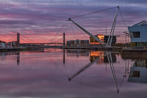 View of tidal river with footbridge and university building at sunrise