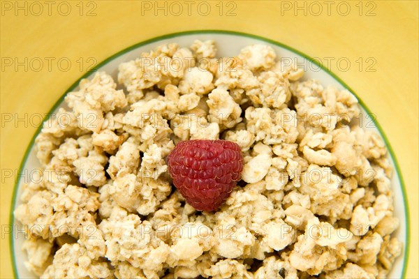 Granola cereal with raspberry in a yellow bowl