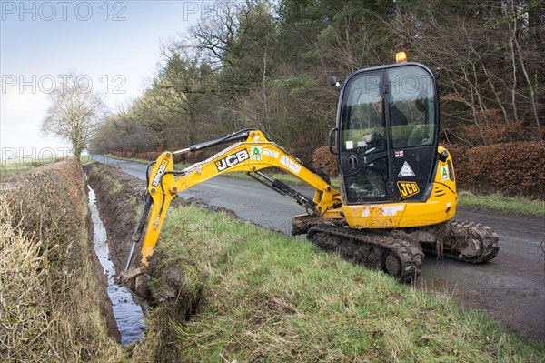 Cleaning overgrown roadside drainage ditches with a JCB excavator