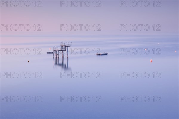 Rosa-violette Abendstimmung ueber dem Bodensee mit Blick zum Sprungturm und den Flossen der Freibadanlage Horn inmitten des Sees