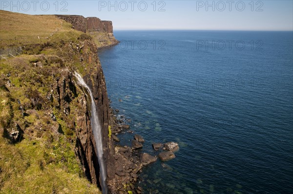 View of the coastline with a waterfall cascading over cliffs into the sea with Kilt Rock in the background