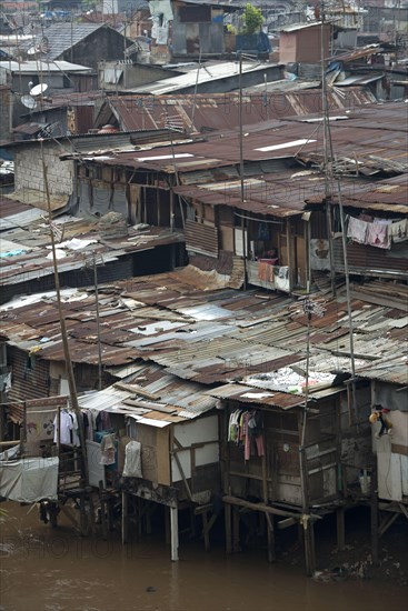 Stilted shacks with corrugated iron roofs beside river in city