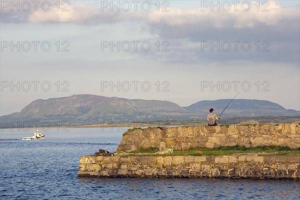 Man rod fishing on summers evening as boat heads out to sea. Sligo