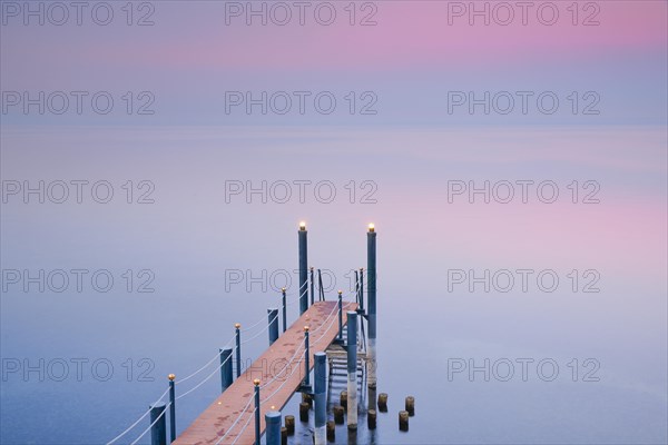 Rosa Abendstimmung ueber dem Bodensee mit beleuchtetem Badesteg zum See