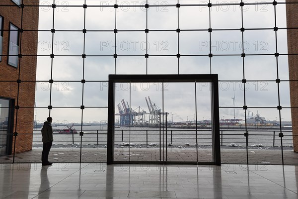 Young man standing in front of modern glass facade with large door and looking at the harbour