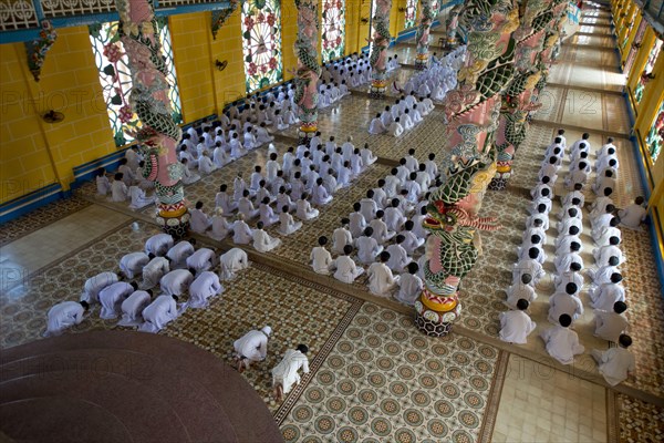 Caodaist disciples sitting beside colourful columns with dragons during ceremony