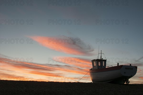 Fishing boat hauled up on shingle beach at sunset