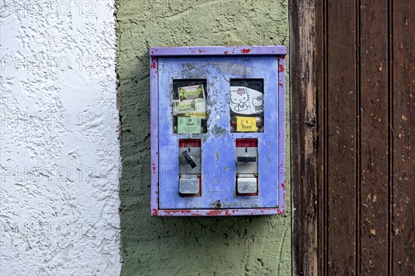 Old chewing gum machine filled with chewing gum and children's toys on the wall of a house