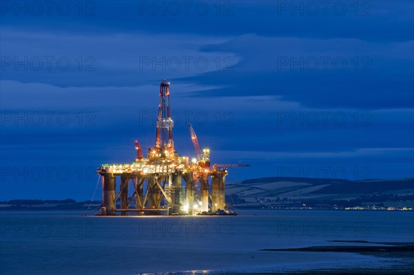 Oil rig moored in sea near coast at night