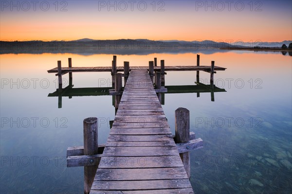 Holzsteg am Pfaeffikersee im Gegenlicht bei Sonnenaufgang mit Blick zum Bachtel und Glaernisch im Hintergrund