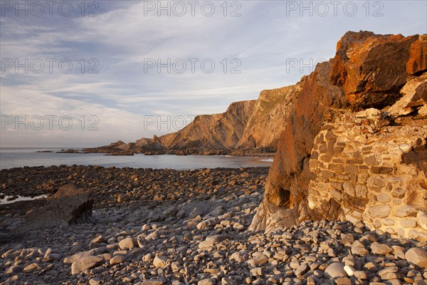Man-made dyke and coastal cliff with folded layers at sunset
