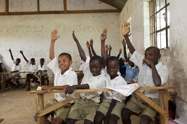 Children with their hands up in the classroom of a rural school