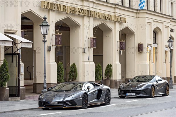 Parked Lamborghini Aventador and Ferrari F12 Berlinetta sports cars in front of Hotel Vier Jahreszeiten Kempinski