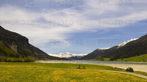 Two bikers at Lake Resia and Ortler Mountains in Val Venosta Alto Adige