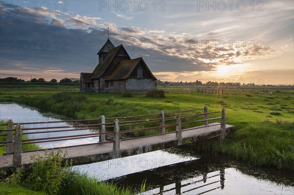 View of grazing moor with footbridge over flooded ditch and church at sunset