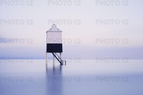 View of low wooden pile lighthouse on beach during rising tide at dawn