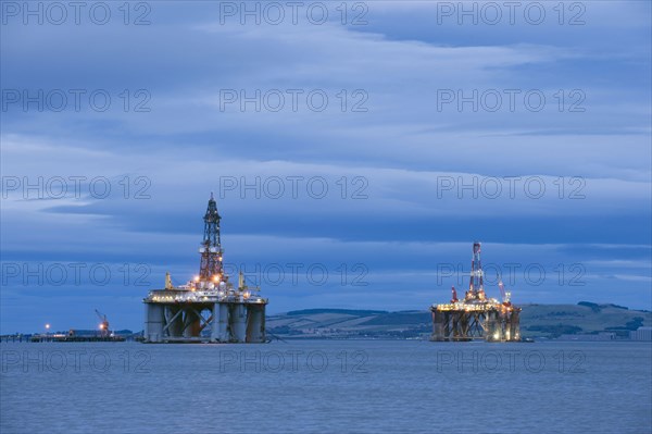 Oil rigs moored in sea near coast at dusk