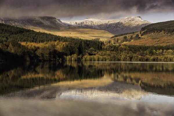 Trees and snow-capped hills reflected in the reservoir at sunrise