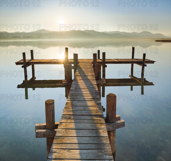 Holzsteg am Pfaeffikersee im Gegenlicht bei Sonnenaufgang mit Blick zum Bachtel und Glaernisch im Hintergrund