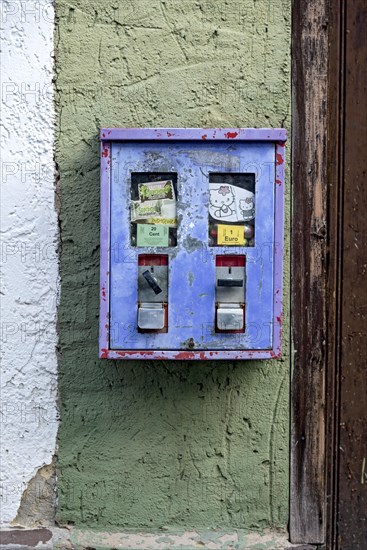 Old chewing gum machine filled with chewing gum and children's toys on the wall of a house