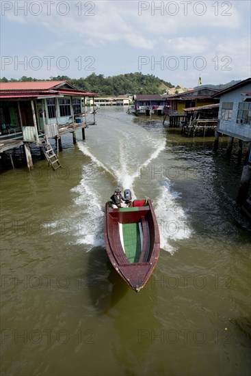 Water taxi speedboat past huts on stilts in the river