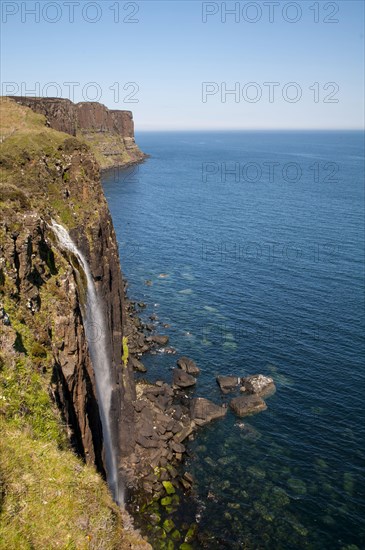 View of the coastline with a waterfall cascading over cliffs into the sea with Kilt Rock in the background