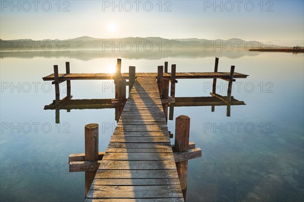 Holzsteg am Pfaeffikersee im Gegenlicht bei Sonnenaufgang mit Blick zum Bachtel und Glaernisch im Hintergrund