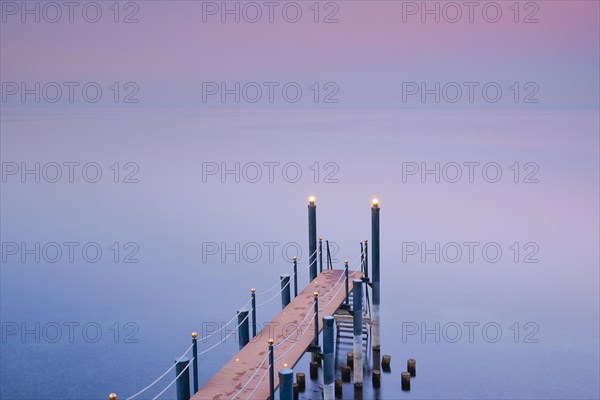 Rosa-violette Abendstimmung ueber dem Bodensee mit beleuchtetem Badesteg zum See