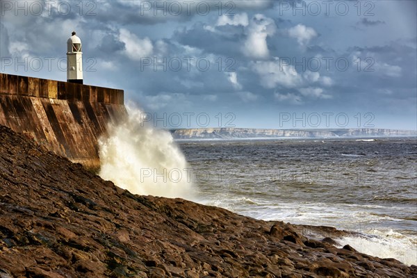 Waves crashing against the seafront and coastal town lighthouse