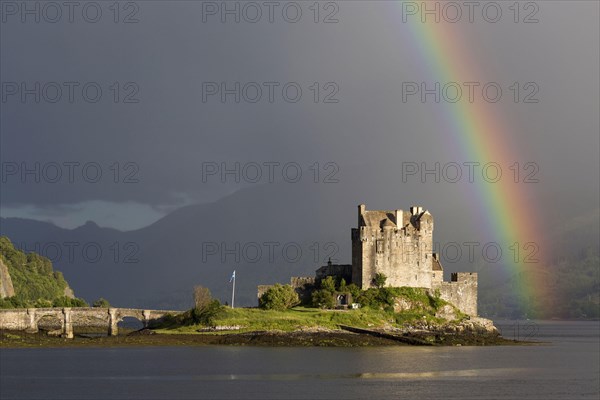 View of restored castle on tidal island in sea loch with rainbow