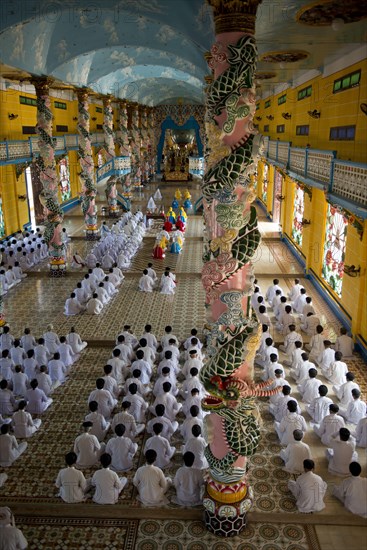 Caodaist disciples sitting beside colourful columns with dragons during ceremony