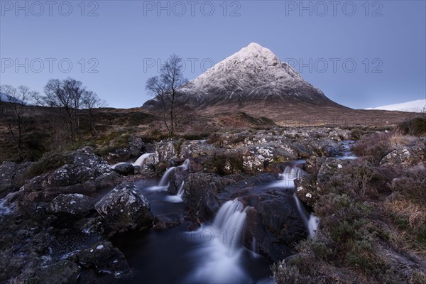 View of moorland with small waterfalls in rocky stream and snow-capped mountain in background at dawn