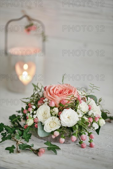 Blumengesteck mit Rosen und Efeu stehen auf altem weissen Holzbrett