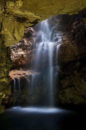 Waterfall flowing through sinkhole into cave