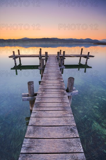 Holzsteg am Pfaeffikersee im Gegenlicht bei Sonnenaufgang mit Blick zum Bachtel und Glaernisch im Hintergrund