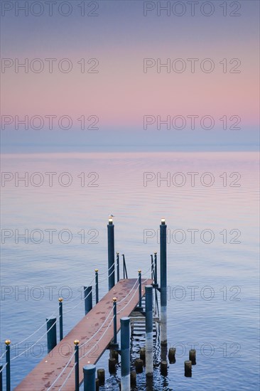 Rosa Abendstimmung ueber dem Bodensee mit beleuchtetem Badesteg zum See