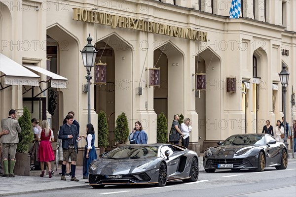 Parked Lamborghini Aventador and Ferrari F12 Berlinetta sports cars in front of Hotel Vier Jahreszeiten Kempinski