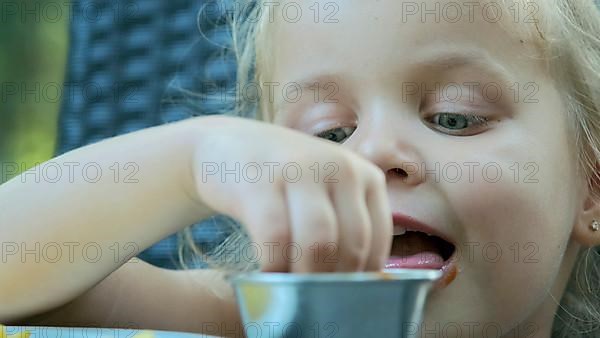 Little girl eat french fries. Close-up of blonde girl takes potato chips with her hands and tries them sitting in street cafe on the park. Odessa