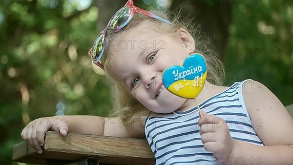 Little blonde girl holds gingerbread in Ukrainian national colors in her hand