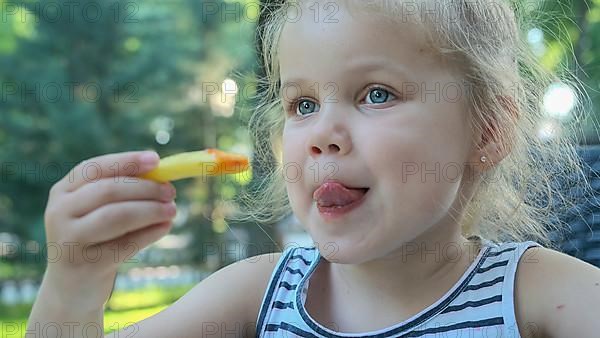 Little girl eat french fries. Close-up of blonde girl takes potato chips with her hands and tries them sitting in street cafe on the park. Odessa