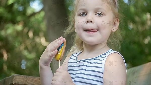 Little blonde girl holds gingerbread in Ukrainian national colors in her hand