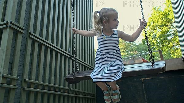 Smiles little rides on swing. Close-up of a blonde girl is swinging on swing in city park. Odessa Ukraine